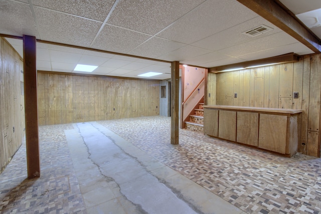 finished below grade area with stairs, visible vents, a drop ceiling, and wood walls