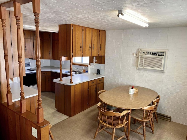 kitchen featuring light countertops, a wall unit AC, a sink, brown cabinetry, and electric range