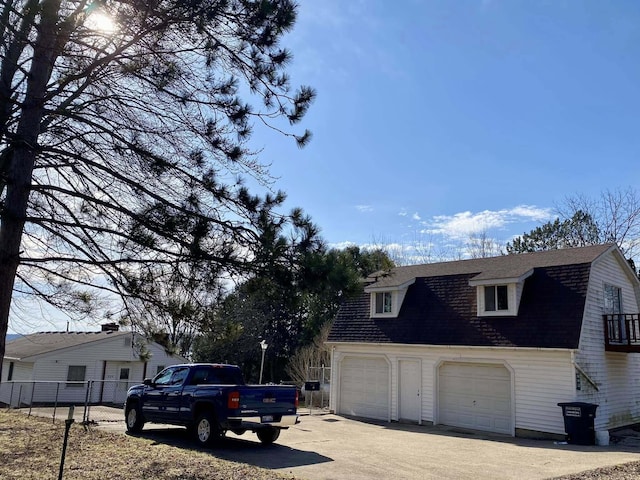 view of home's exterior with roof with shingles, a gambrel roof, fence, and driveway