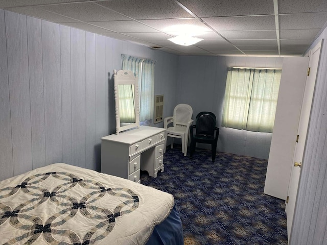 bedroom with wood walls, dark colored carpet, a paneled ceiling, and multiple windows