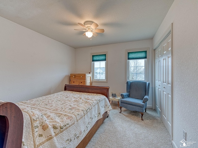 bedroom with a closet, light carpet, a textured ceiling, ceiling fan, and a textured wall