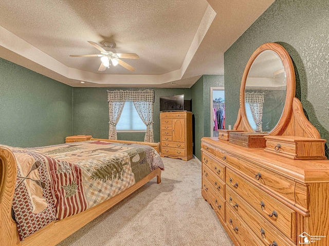 bedroom with light colored carpet, a ceiling fan, a textured ceiling, and a raised ceiling