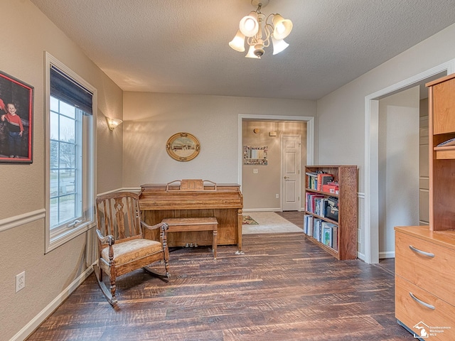 living area featuring a notable chandelier, dark wood-style floors, baseboards, and a textured ceiling