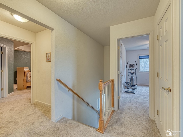 hall with an upstairs landing, carpet flooring, a textured wall, baseboards, and a textured ceiling