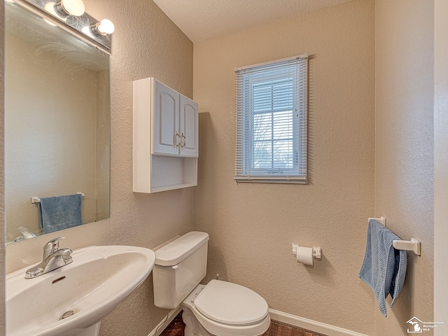 half bath with a textured wall, baseboards, a sink, and toilet