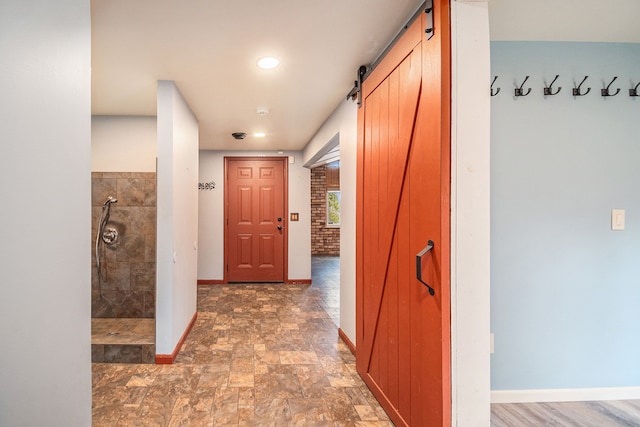 corridor with recessed lighting, a barn door, stone finish floor, and baseboards