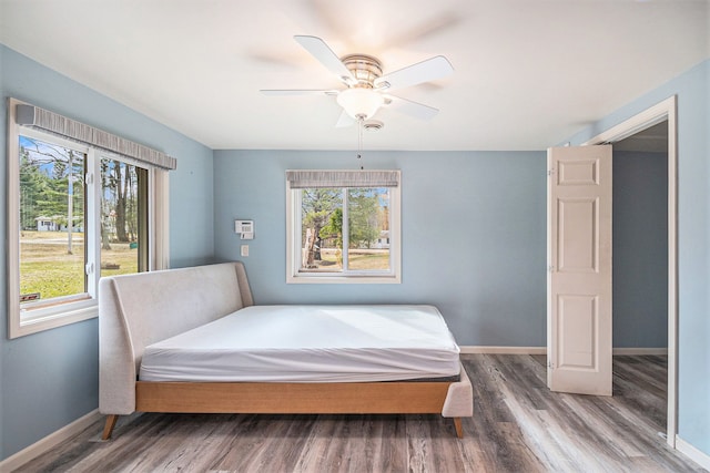 bedroom with wood finished floors, baseboards, and multiple windows