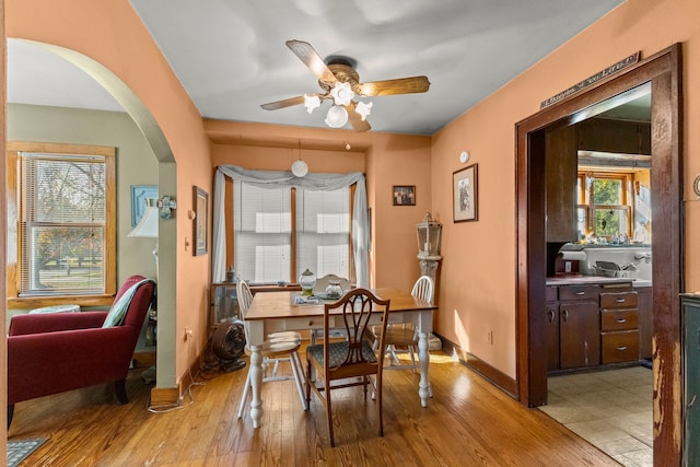 dining space featuring light wood-type flooring, arched walkways, baseboards, and ceiling fan