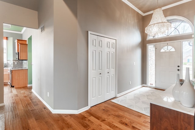 foyer featuring a towering ceiling, light wood-style floors, crown molding, and visible vents