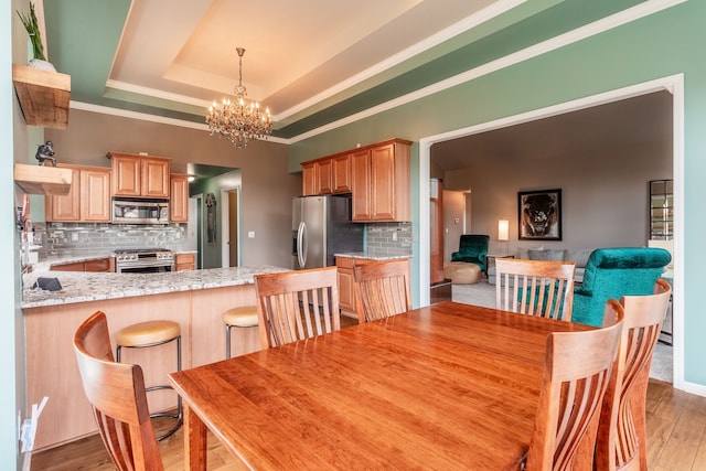 dining room with a chandelier, crown molding, light wood finished floors, and a tray ceiling