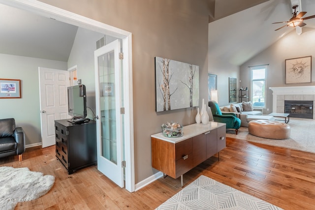 living room featuring light wood-style flooring, ceiling fan, a fireplace, baseboards, and high vaulted ceiling