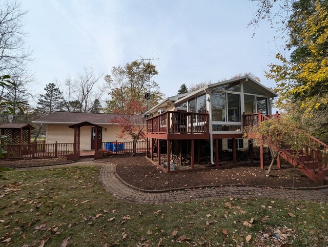 rear view of property featuring stairs, a wooden deck, a sunroom, and a yard