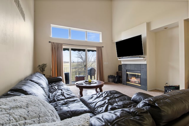 living area with a fireplace, visible vents, a towering ceiling, and carpet flooring