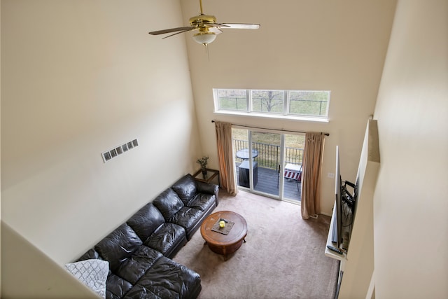 carpeted living area with a high ceiling, ceiling fan, and visible vents