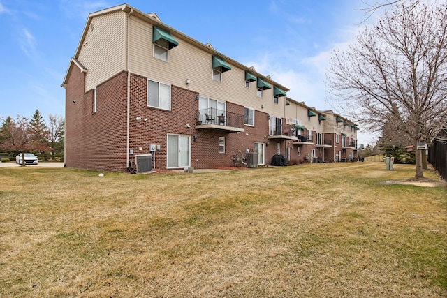 back of house featuring a lawn, cooling unit, and brick siding