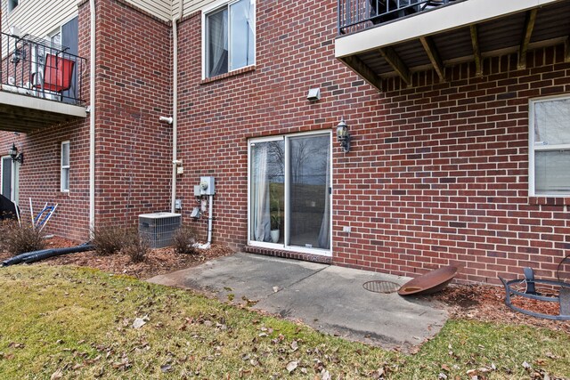 property entrance with brick siding, a balcony, and central AC unit