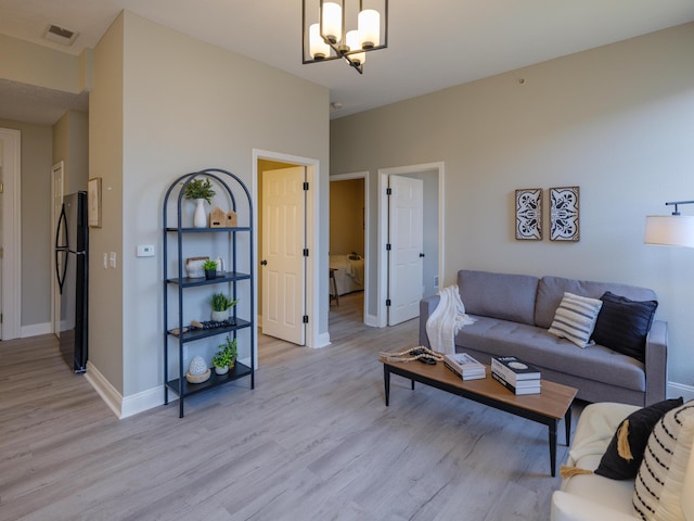 living area with baseboards, visible vents, light wood-style flooring, and an inviting chandelier