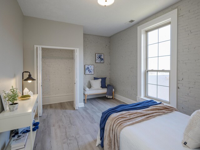 bedroom featuring light wood-style flooring, brick wall, baseboards, and visible vents
