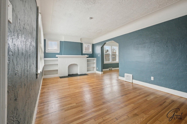 10088 Britain St, Detroit, MI 48224 - unfurnished living room featuring a textured ceiling, visible vents, baseboards, arched walkways, and wood-type flooring