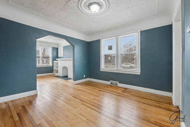 10088 Britain St, Detroit, MI 48224 - unfurnished living room featuring a textured ceiling, visible vents, hardwood / wood-style flooring, baseboards, and arched walkways