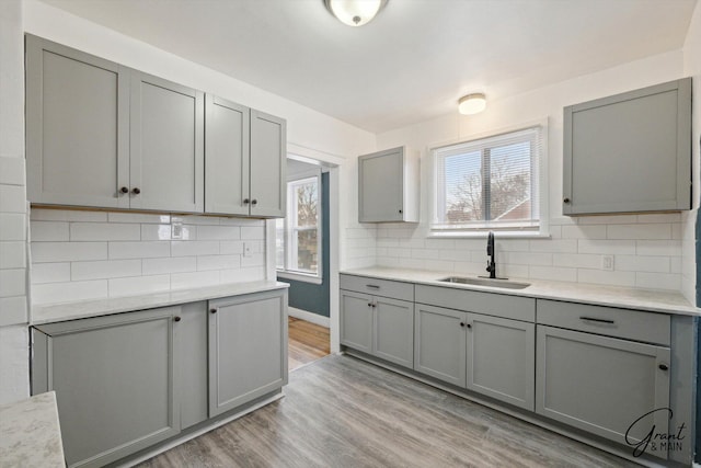 10088 Britain St, Detroit, MI 48224 - kitchen featuring light countertops, gray cabinetry, decorative backsplash, a sink, and light wood-style flooring