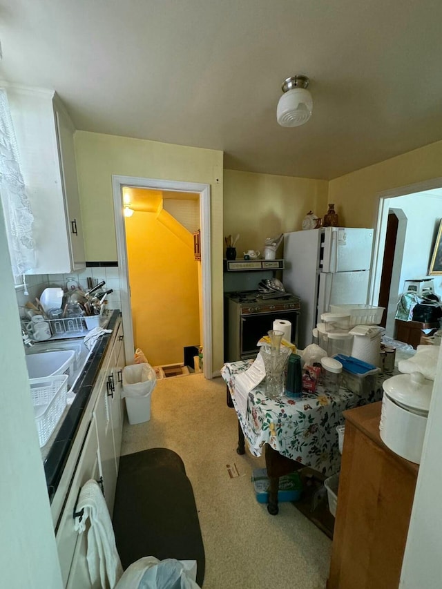 kitchen with decorative backsplash, carpet flooring, white cabinets, a sink, and freestanding refrigerator