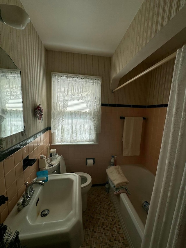 full bathroom with wallpapered walls, toilet, a sink, and wainscoting
