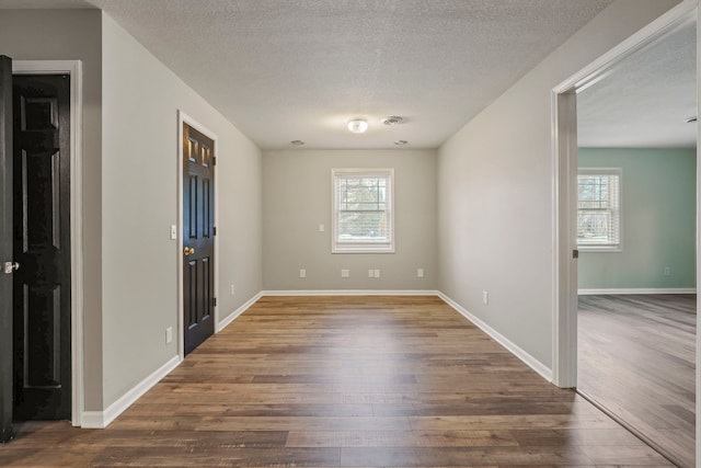 unfurnished room with a textured ceiling, baseboards, and wood finished floors