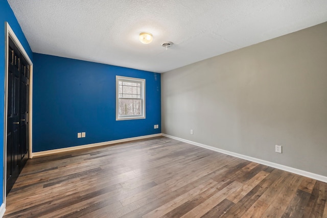 unfurnished bedroom with a closet, a textured ceiling, visible vents, baseboards, and wood finished floors