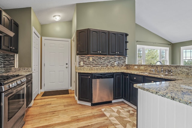 kitchen with light stone countertops, a sink, stainless steel appliances, and lofted ceiling