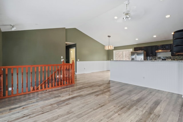 unfurnished living room with a wainscoted wall, vaulted ceiling, light wood-type flooring, recessed lighting, and an inviting chandelier