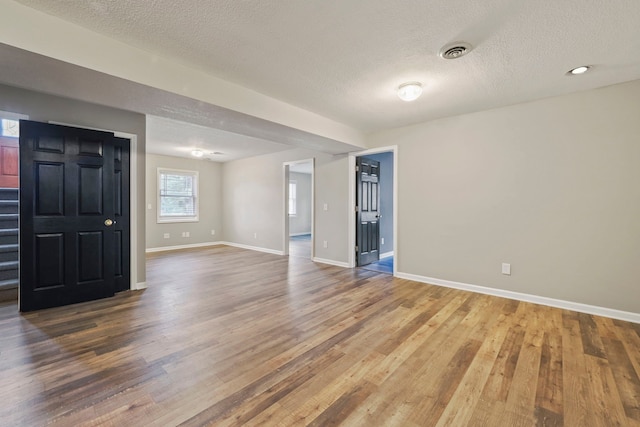 empty room featuring baseboards, visible vents, a textured ceiling, and wood finished floors