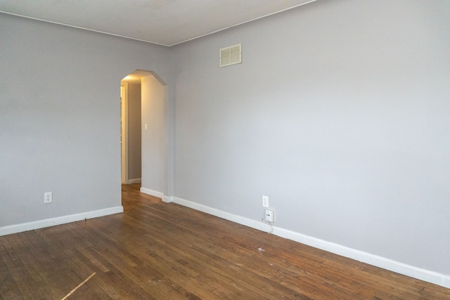 empty room featuring baseboards, visible vents, arched walkways, and hardwood / wood-style floors