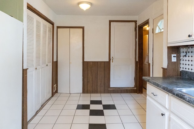 kitchen with white cabinets, dark countertops, wood walls, and wainscoting