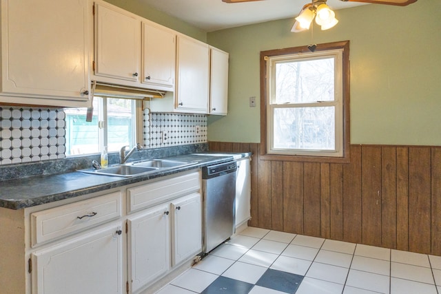 kitchen with a wainscoted wall, a sink, dark countertops, and dishwasher