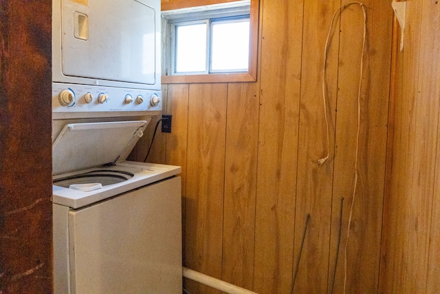 laundry area featuring wood walls and stacked washing maching and dryer