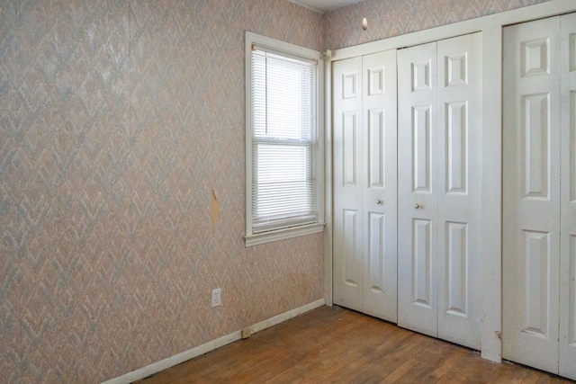 unfurnished bedroom with wallpapered walls, baseboards, and wood finished floors