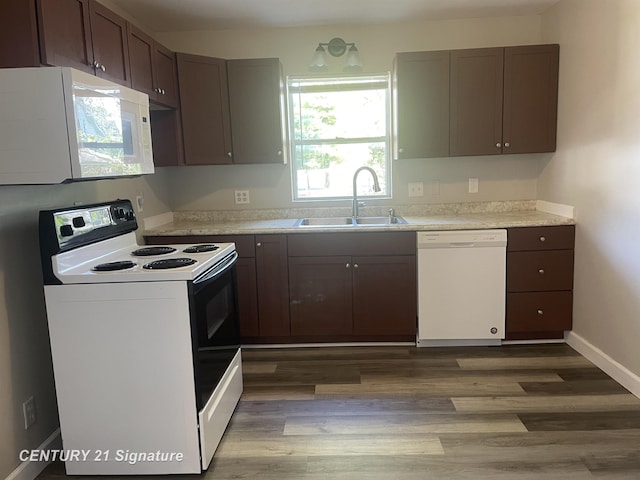 kitchen featuring light countertops, light wood finished floors, baseboards, white appliances, and a sink