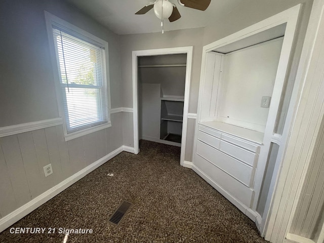 unfurnished bedroom featuring a wainscoted wall, visible vents, a ceiling fan, and dark colored carpet