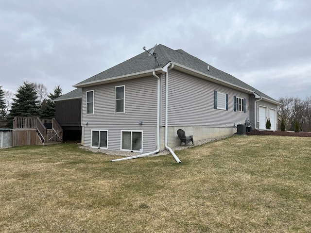 back of house with central AC unit, a lawn, a shingled roof, and a garage