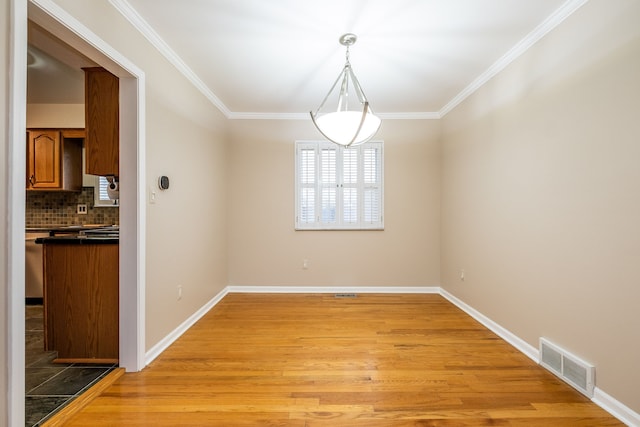 unfurnished dining area with light wood-style flooring, crown molding, baseboards, and visible vents