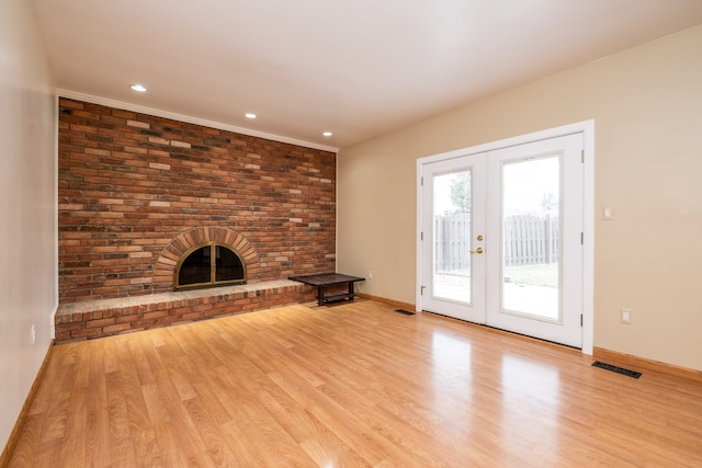 unfurnished living room with visible vents, light wood-style floors, french doors, and a brick fireplace
