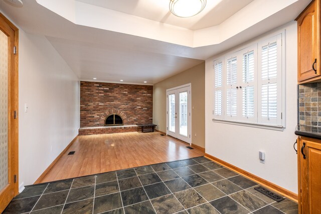 unfurnished living room with baseboards, visible vents, wood finished floors, and a brick fireplace