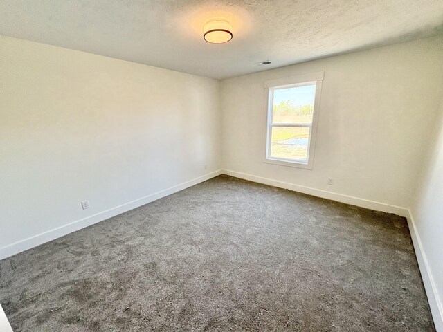 spare room with baseboards, dark carpet, and a textured ceiling