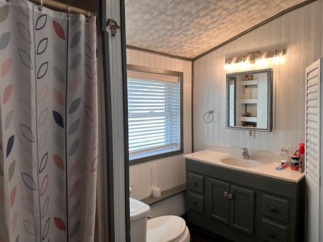 8034 N Johnson Rd, Irons, MI 49644 - full bathroom with crown molding, toilet, vanity, a shower with curtain, and wood walls