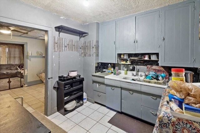 kitchen with light countertops, light tile patterned floors, gray cabinetry, a textured ceiling, and a sink