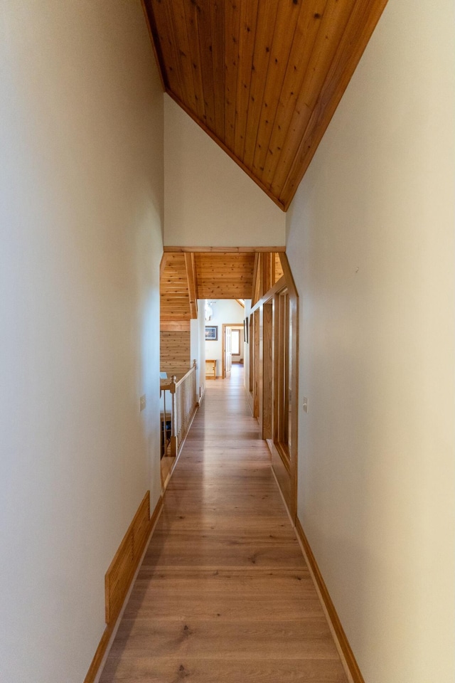 corridor with baseboards, high vaulted ceiling, wooden ceiling, and light wood-style floors
