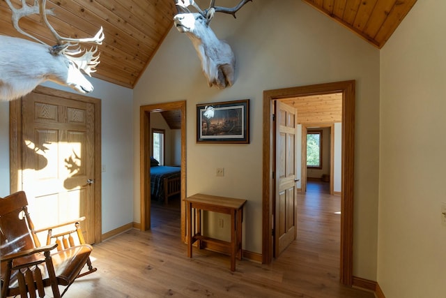 corridor with light wood-style flooring, wooden ceiling, and high vaulted ceiling