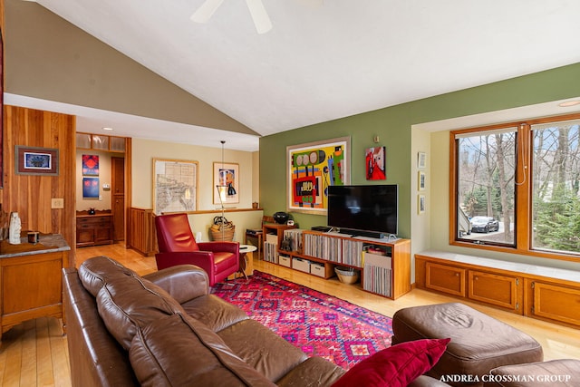 living area featuring lofted ceiling, light wood-style flooring, wood walls, and a ceiling fan