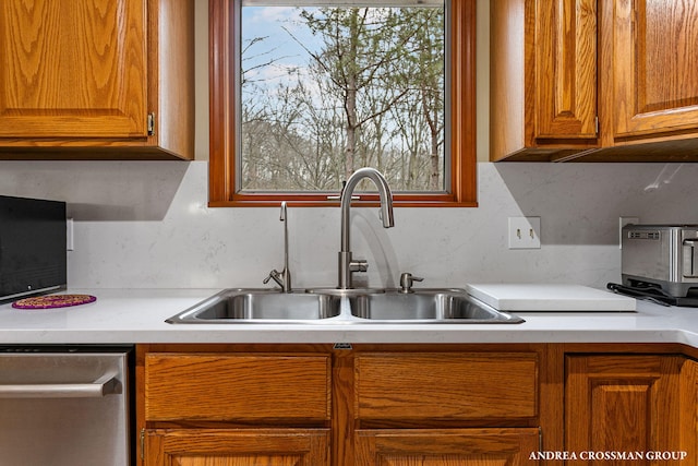 kitchen featuring light countertops, a sink, brown cabinets, and stainless steel dishwasher